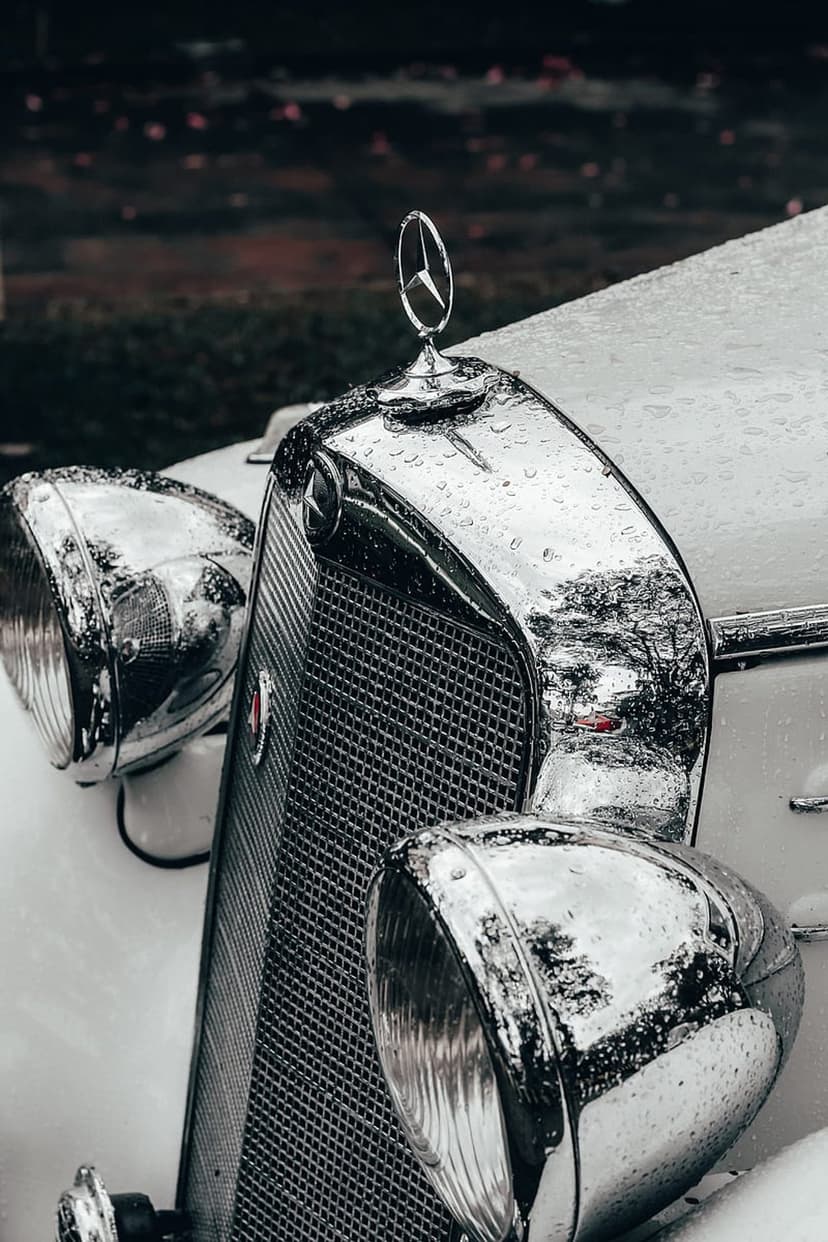Vintage Mercedes-Benz chrome grille and star emblem covered in raindrops under a moody, overcast sky.