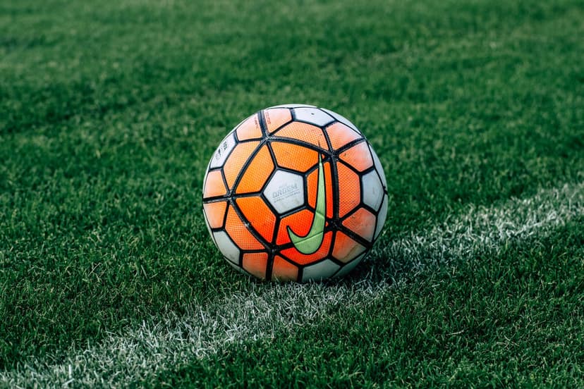Nike soccer ball with orange panels sits on a bright green grass field near a white chalk boundary line during day.