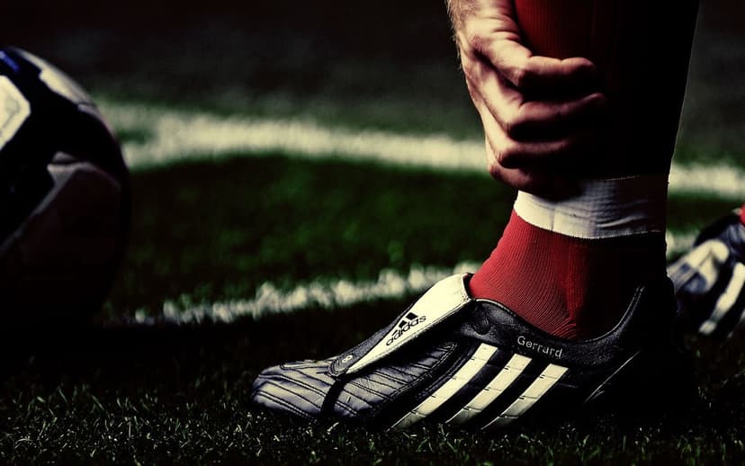 Adidas Predator soccer cleat with Gerrard text sits on a grass field beside a ball in a sharp macro view.