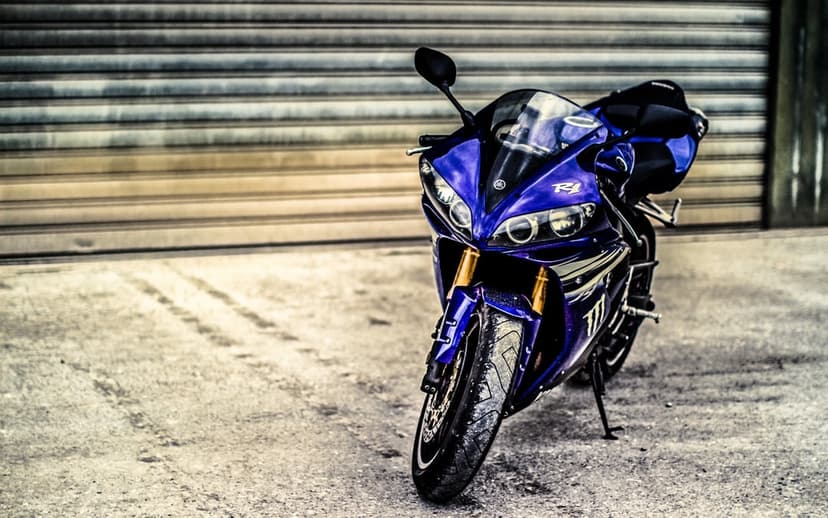 Front view of a blue Yamaha R1 motorcycle with projector headlights and gold forks against a metal garage door.
