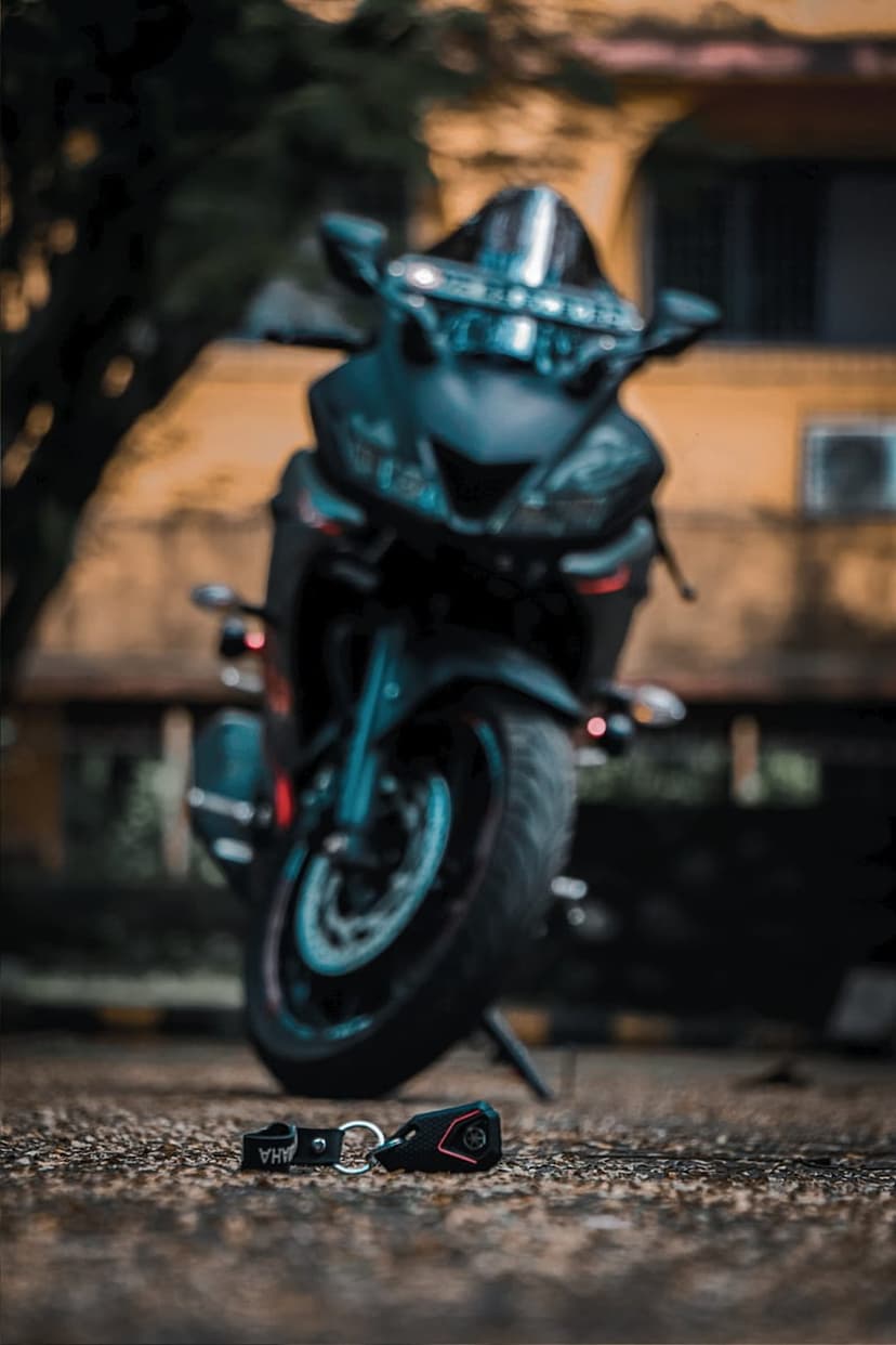 Yamaha ignition keys rest on a gravel surface in front of a black sports motorcycle with a tinted windshield.