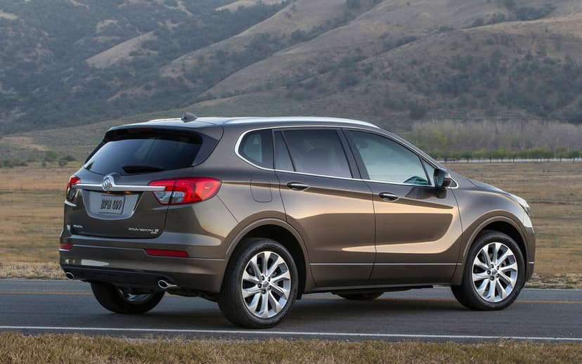 Brown Buick Envision SUV parked on a road with sunlit rolling hills and distant mountains in the background.