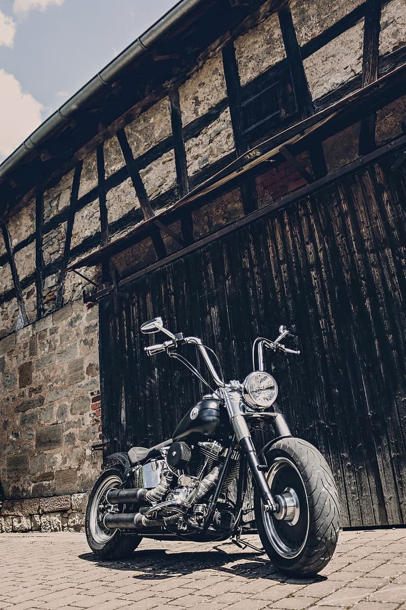 Black Harley Davidson cruiser with chrome parked on a brick path before a weathered timber-framed barn.