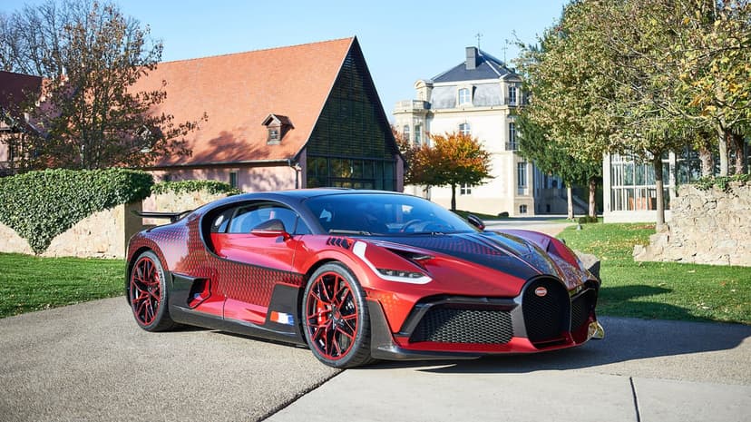 Red Bugatti Divo with a black diamond pattern parked on a driveway in front of a classic European mansion.
