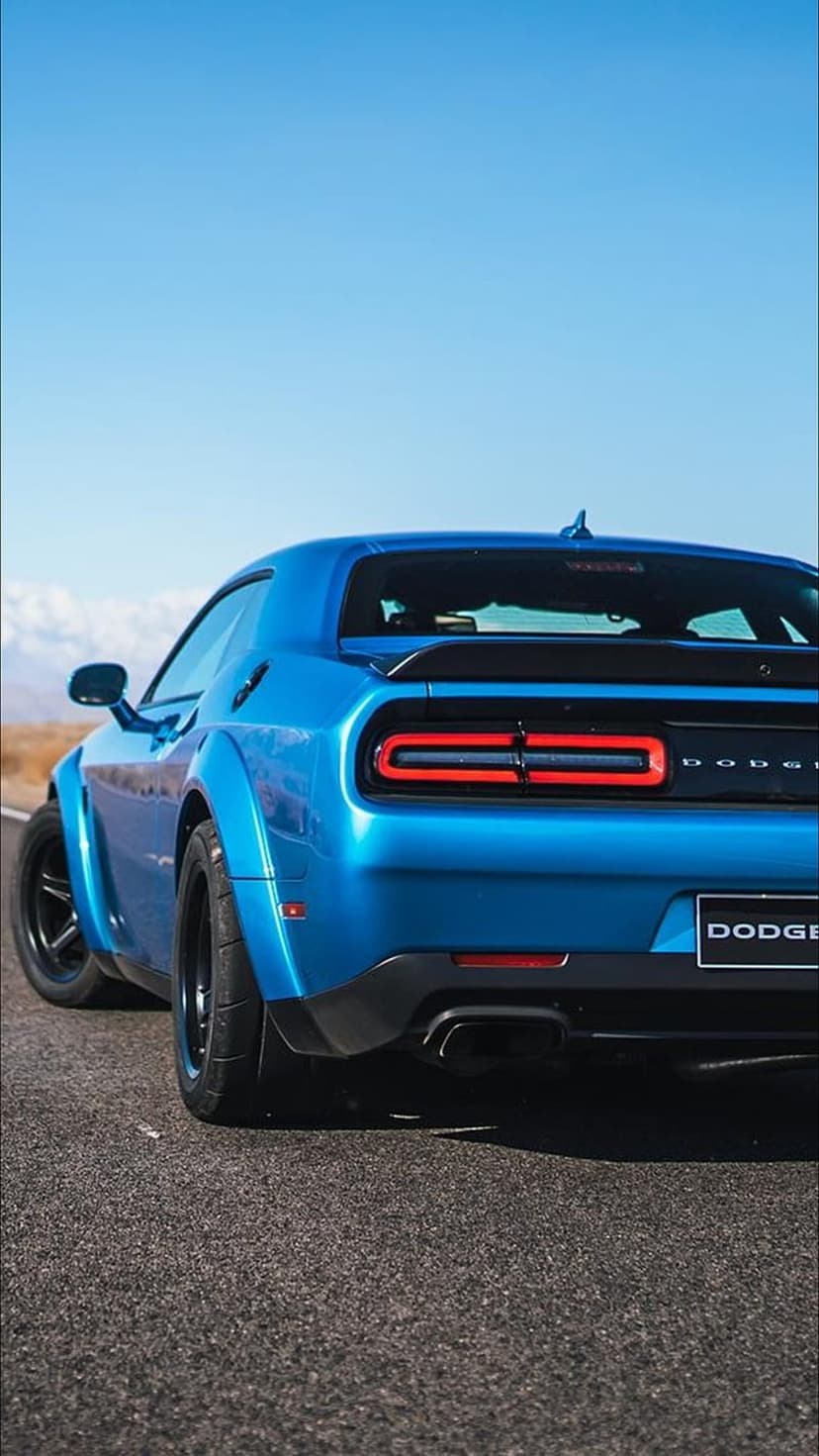 Blue Dodge Challenger widebody rear view featuring glowing red LED tail lights and chrome lettering on a road.