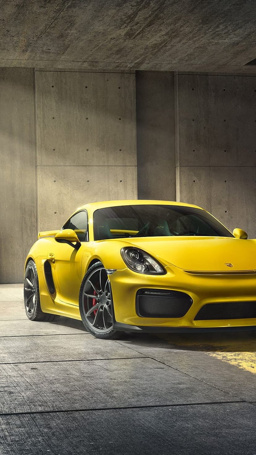 Porsche Cayman GT4 in yellow parked on a textured concrete floor inside a minimalist industrial garage.