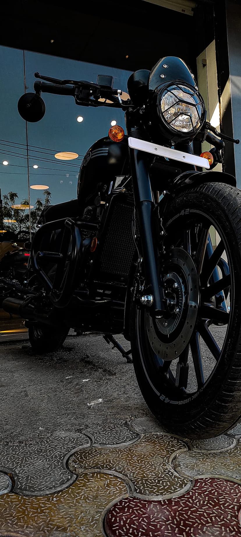 Black Jawa motorcycle with a grilled headlight and orange indicators parked on a yellow and grey stone pavement.