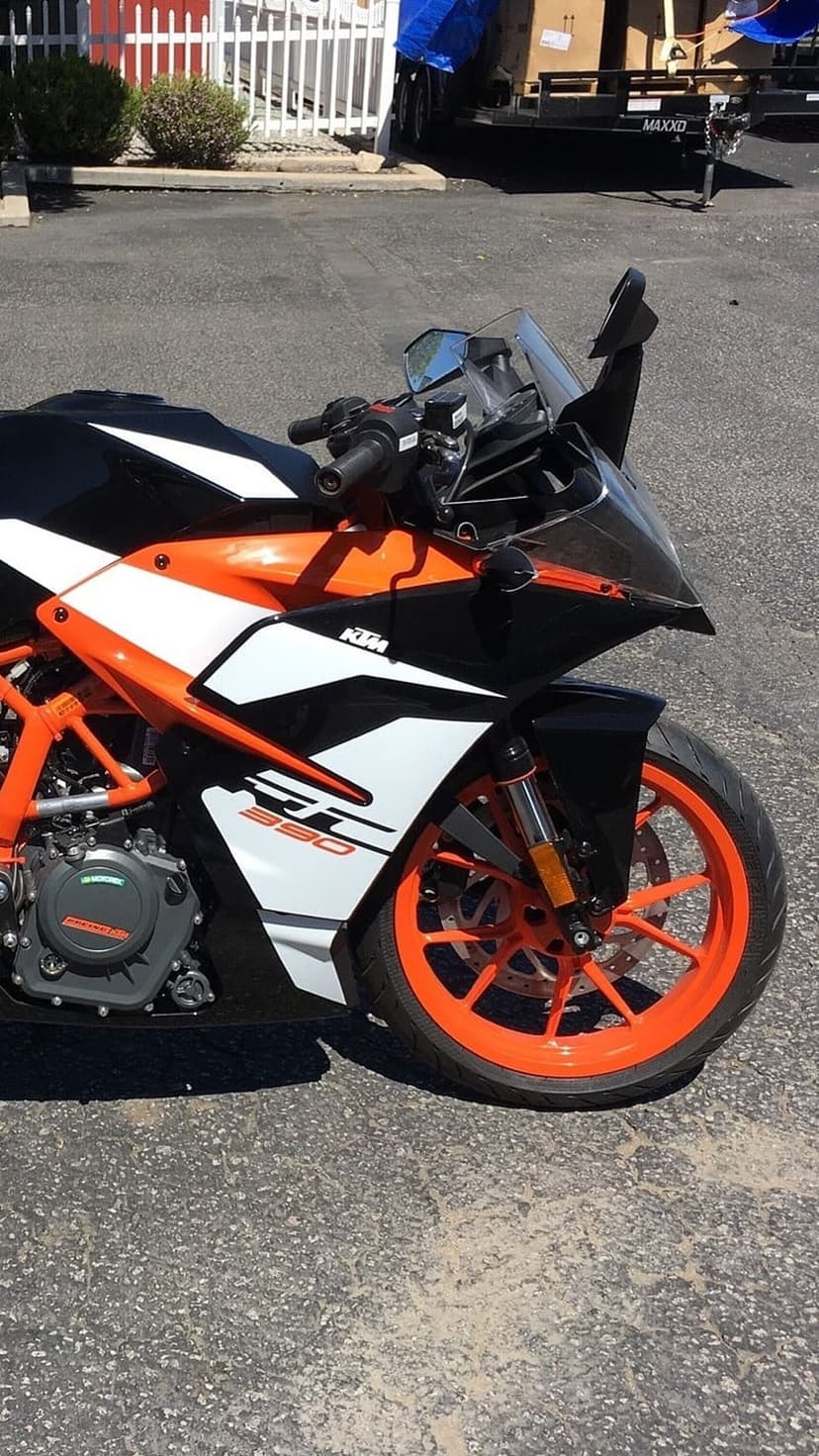 KTM 390 Duke motorcycle front section with orange wheels, white fairings, and 390 graphics on outdoor asphalt.