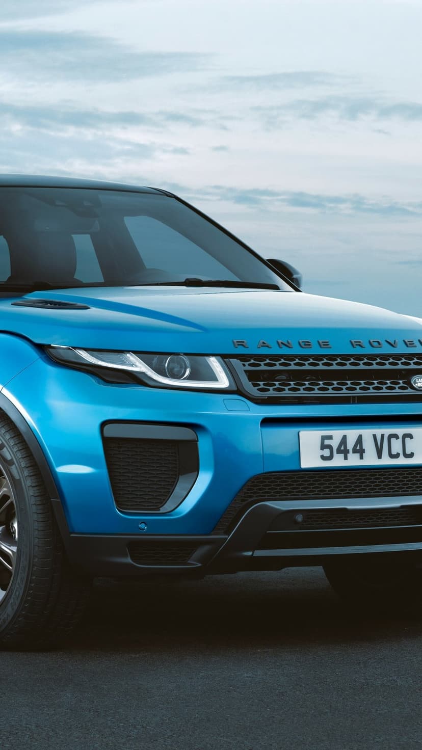 Front profile of a blue Range Rover Evoque with LED headlights and honeycomb grille under a cloudy sky.