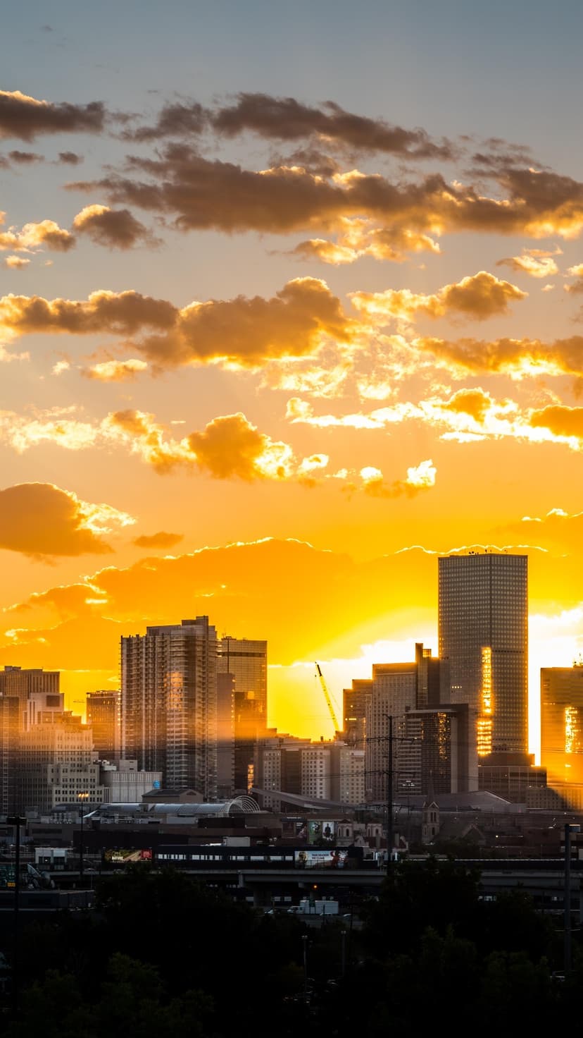 Silhouetted high-rise buildings stand against a fiery orange sunset with glowing clouds in a vertical view.
