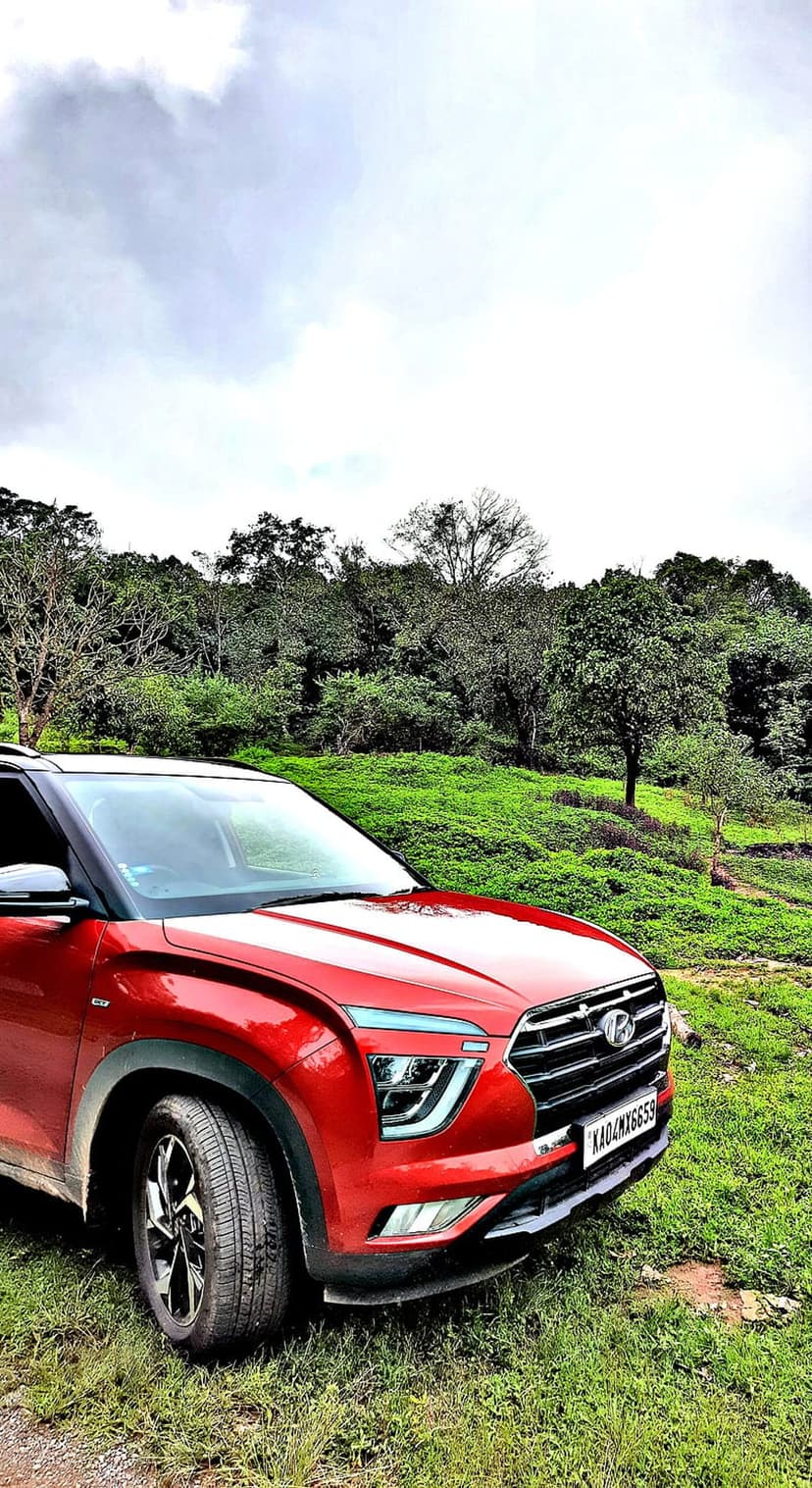 Red Hyundai Creta SUV parked on a grassy slope with a background of dense green trees under an overcast sky.