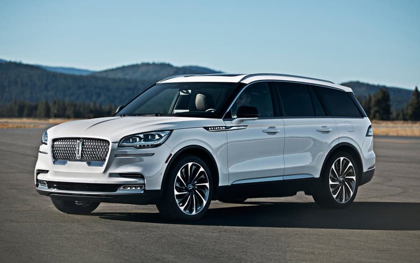 White Lincoln Aviator SUV on an asphalt runway with blue mountains and a clear sky in the background.