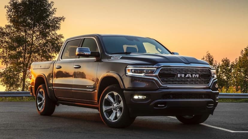 Dark grey Ram 1500 Limited truck on asphalt during a golden sunset with chrome detailing and distant trees.