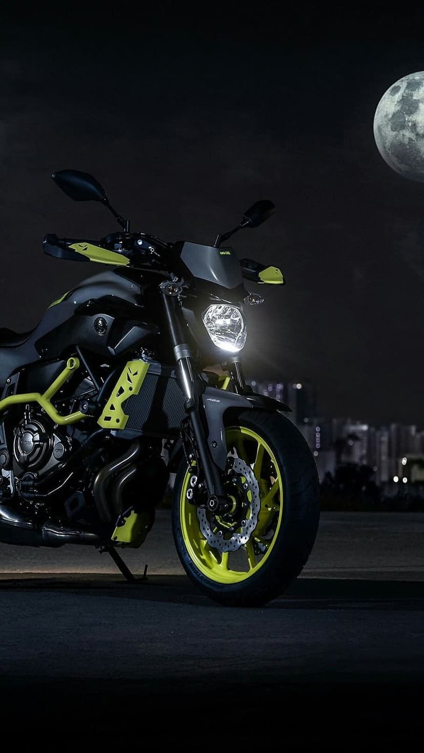 Neon yellow sportbike parked on a dark city street beneath a large full moon and glowing skyscraper lights.