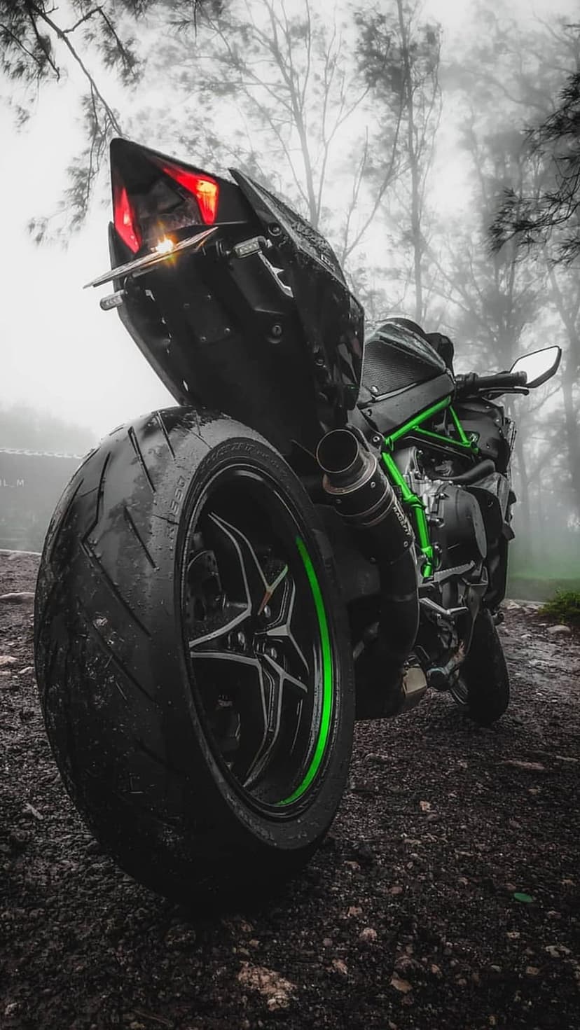 Kawasaki H2R motorcycle with green accents parked on a wet road in a dense, misty forest during a dark day.