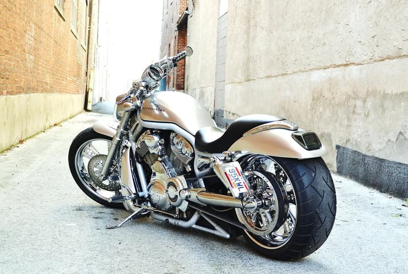 Silver Harley-Davidson V-Rod motorcycle with a wide tire and chrome engine in a narrow urban brick alleyway.