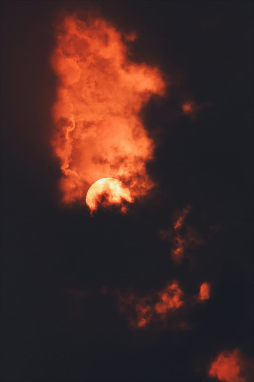 Glowing sun peeking through dark red clouds with intense orange light and dramatic silhouetted atmospheric edges.