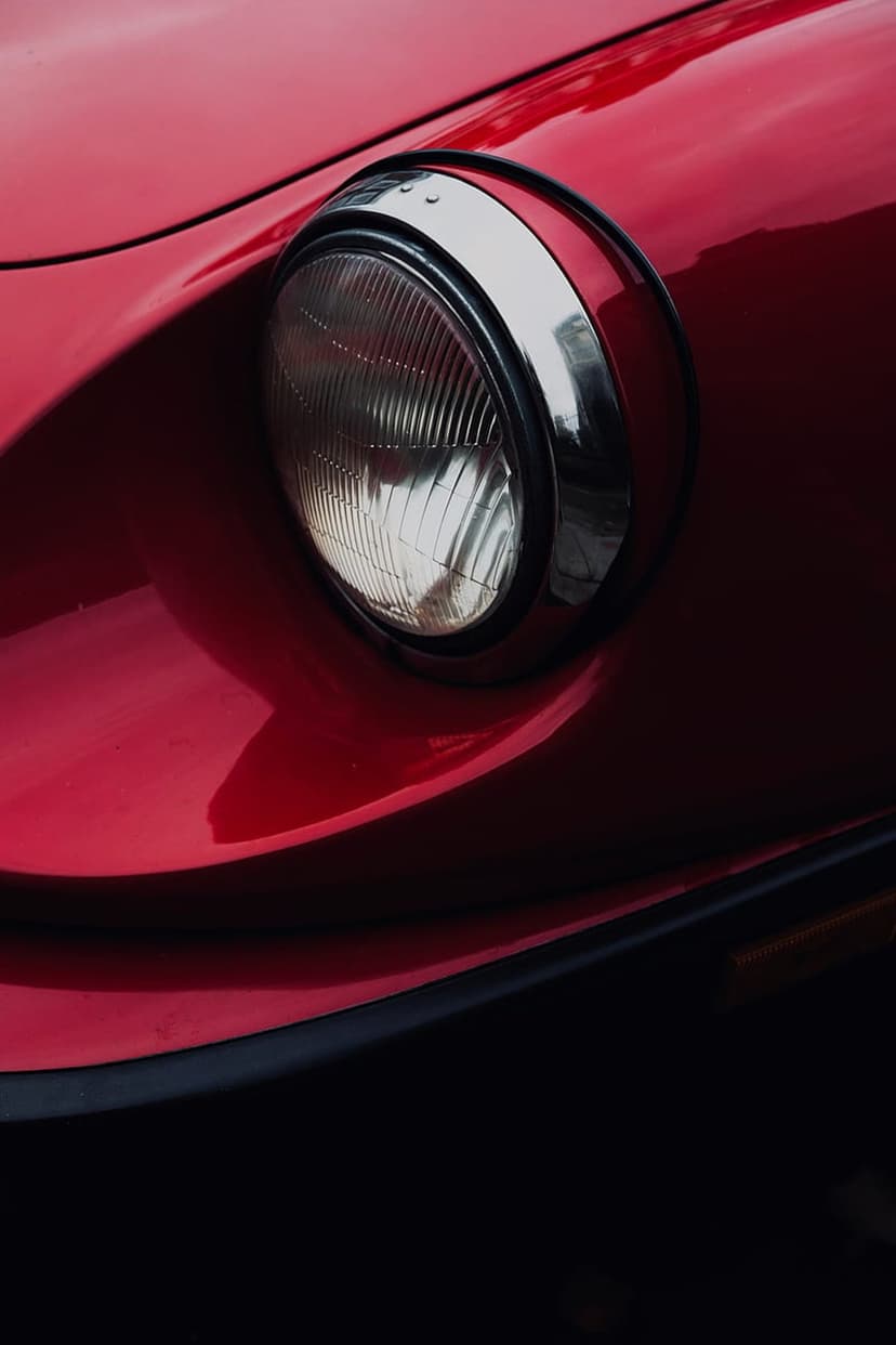 Vintage red car headlight with a geometric glass pattern and polished chrome trim against scarlet paint.