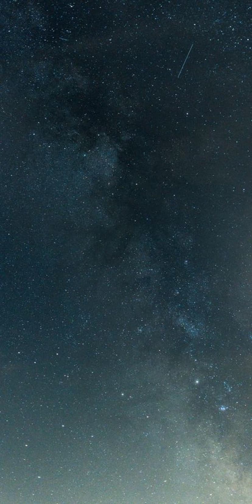 Milky Way galaxy with a bright shooting star and a warm light gradient at the base of the vertical night sky.