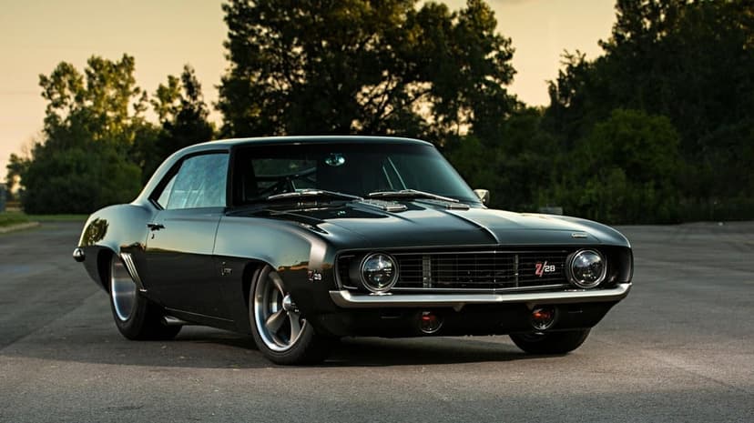 Black 1969 Chevrolet Camaro Z28 muscle car parked on asphalt at sunset with warm golden hour lighting.