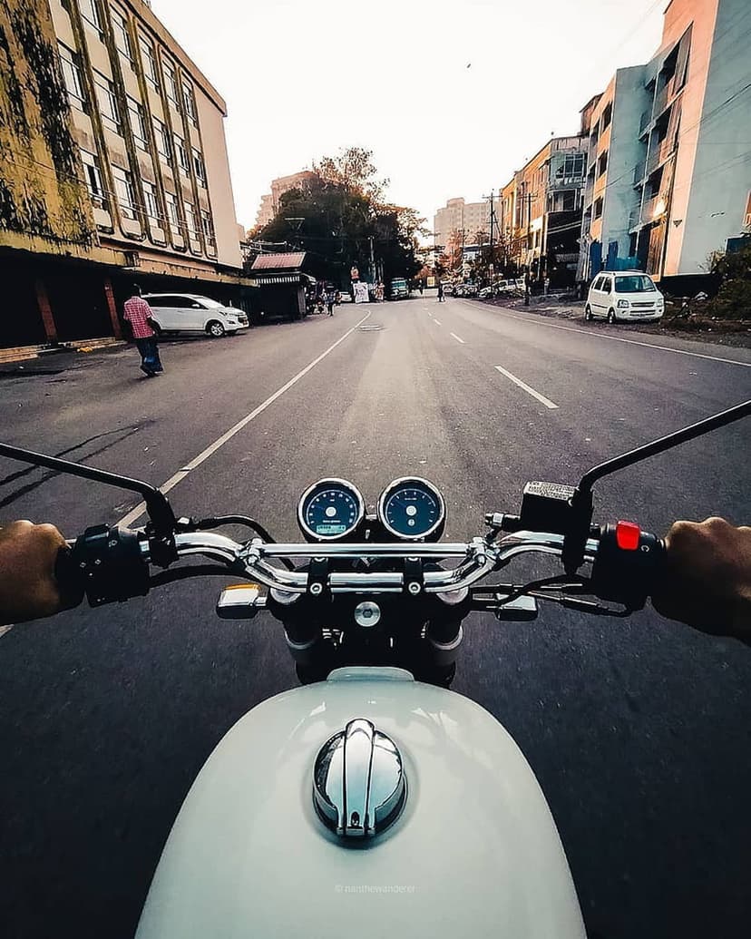 Hands on motorcycle handlebars during a sunset ride through city streets with a golden sky and urban traffic.
