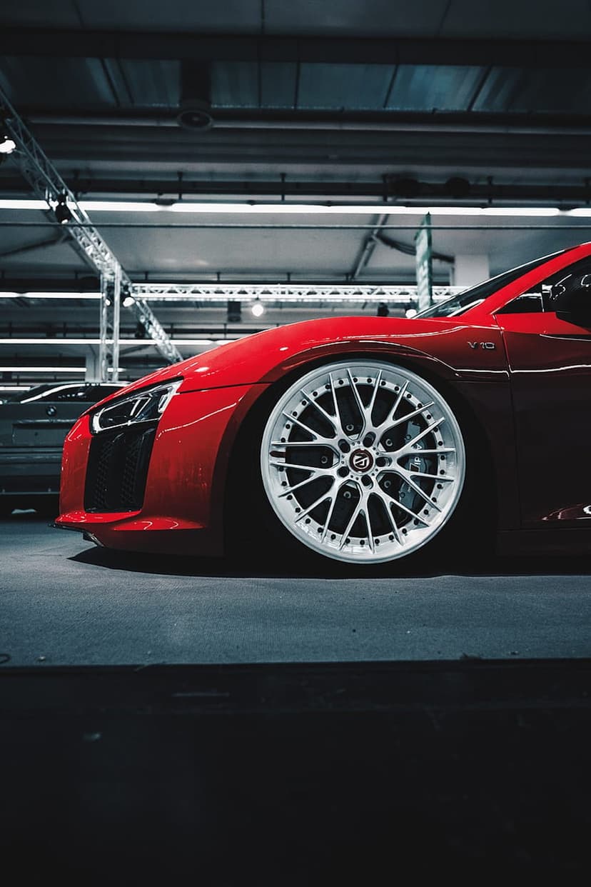 Red sports car wheel with silver multi-spoke rims shown from a low angle under bright indoor exhibition lights.