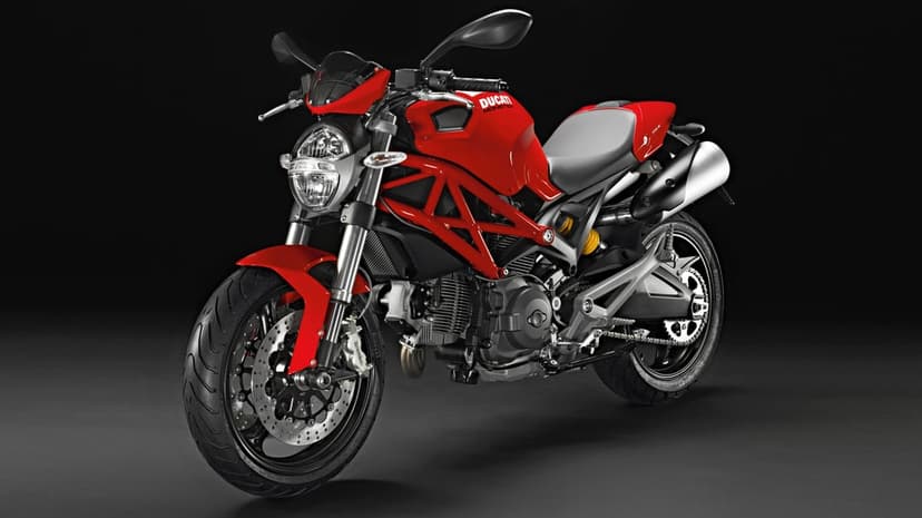 Red Ducati Monster motorcycle with a red trellis frame and silver exhaust against a dark studio background.