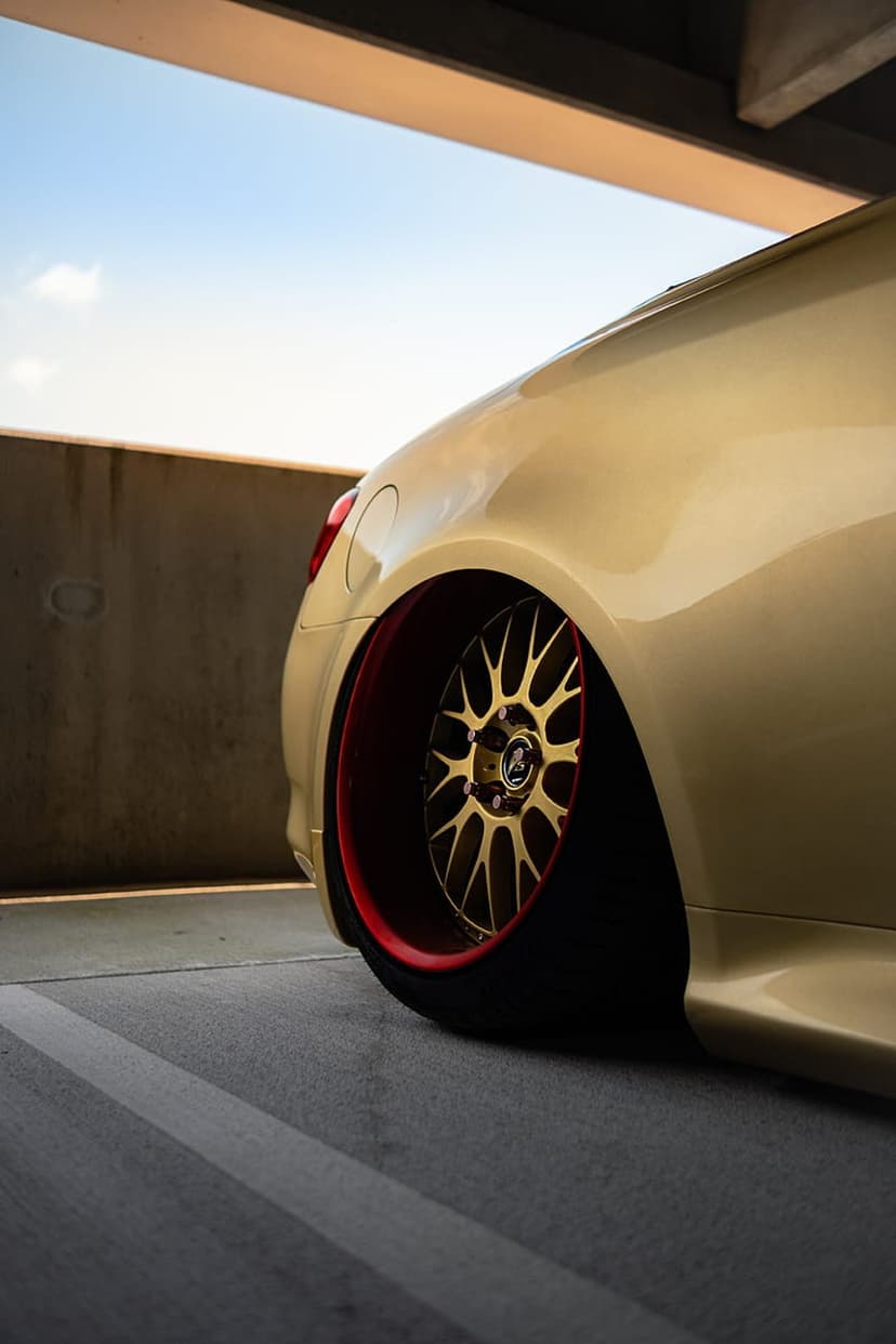 Gold car rear wheel with a red lip rim and slammed suspension parked against a concrete garage wall.
