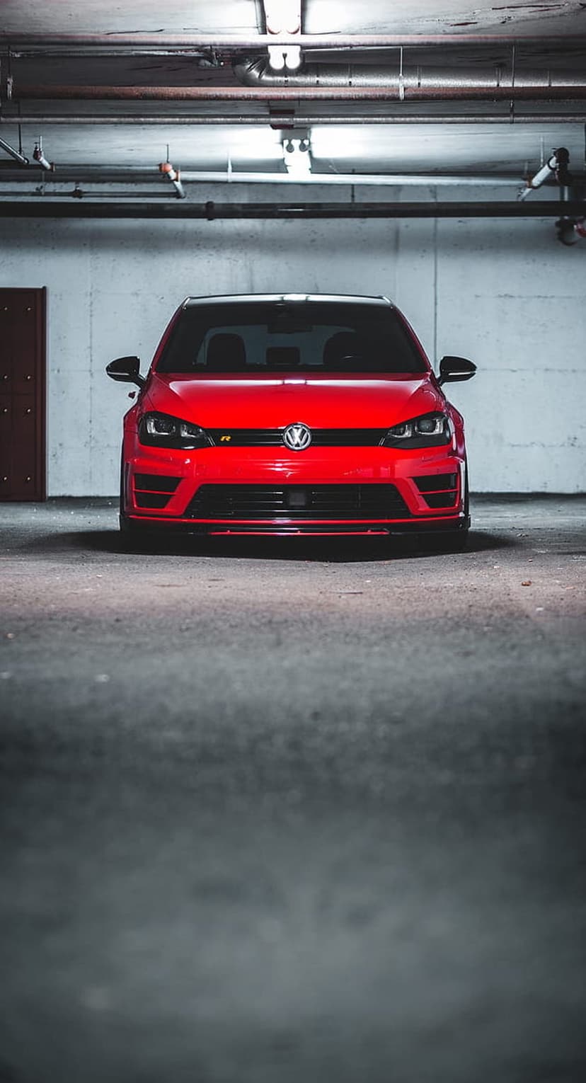 Red Volkswagen Golf R parked in a dimly lit industrial garage with concrete walls and visible overhead pipes.