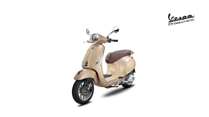 Beige Vespa Primavera scooter with a brown seat and chrome mirrors on a minimalist white background.