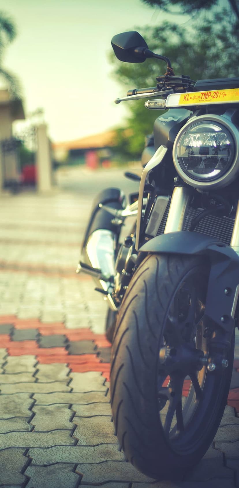 Modern motorcycle with a round headlight and front tire on red stone pavers with a blurred urban background.