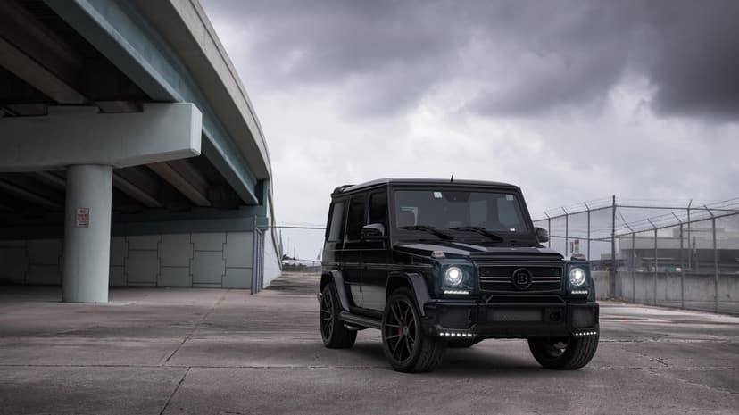 Black Brabus G-Class SUV with glowing LED lights parked on concrete under a bridge beneath a cloudy sky.