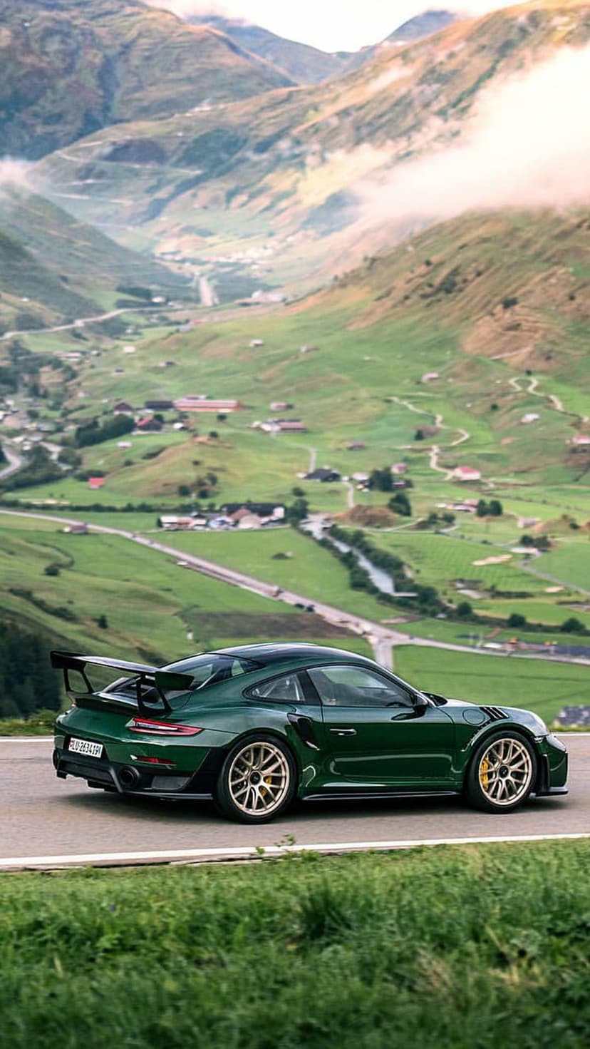 Emerald green Porsche 911 GT2 RS with gold rims drives along a winding mountain road through misty green hills.