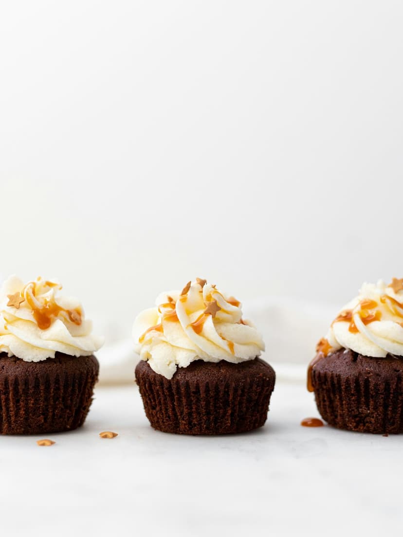 Chocolate cupcakes with swirled white frosting and caramel sauce drizzle against a soft-focus background.