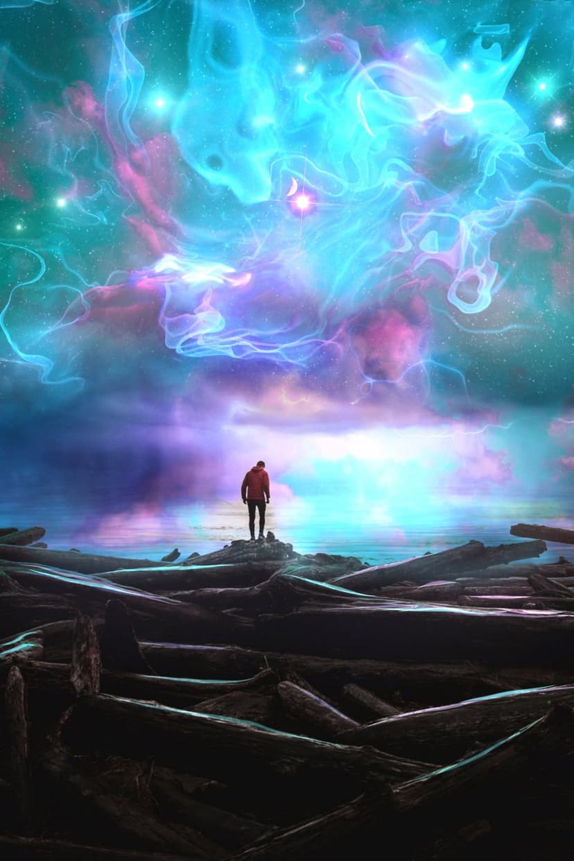 Man in a red jacket stands on driftwood watching a purple and blue cosmic nebula reflect in the ocean water.