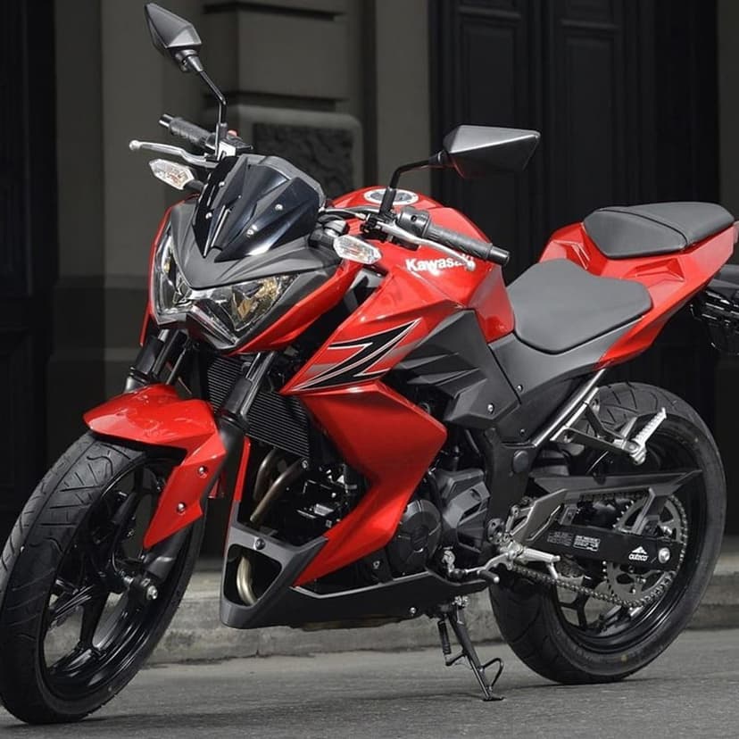 Red Kawasaki Z250 motorcycle featuring sharp fairings and black accents parked on pavement with urban bokeh.