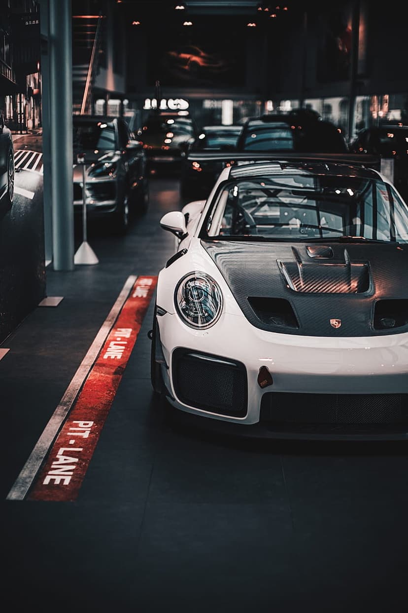 White Porsche 911 GT2 RS with a carbon fiber hood parked on a dark showroom floor with red and white markings.