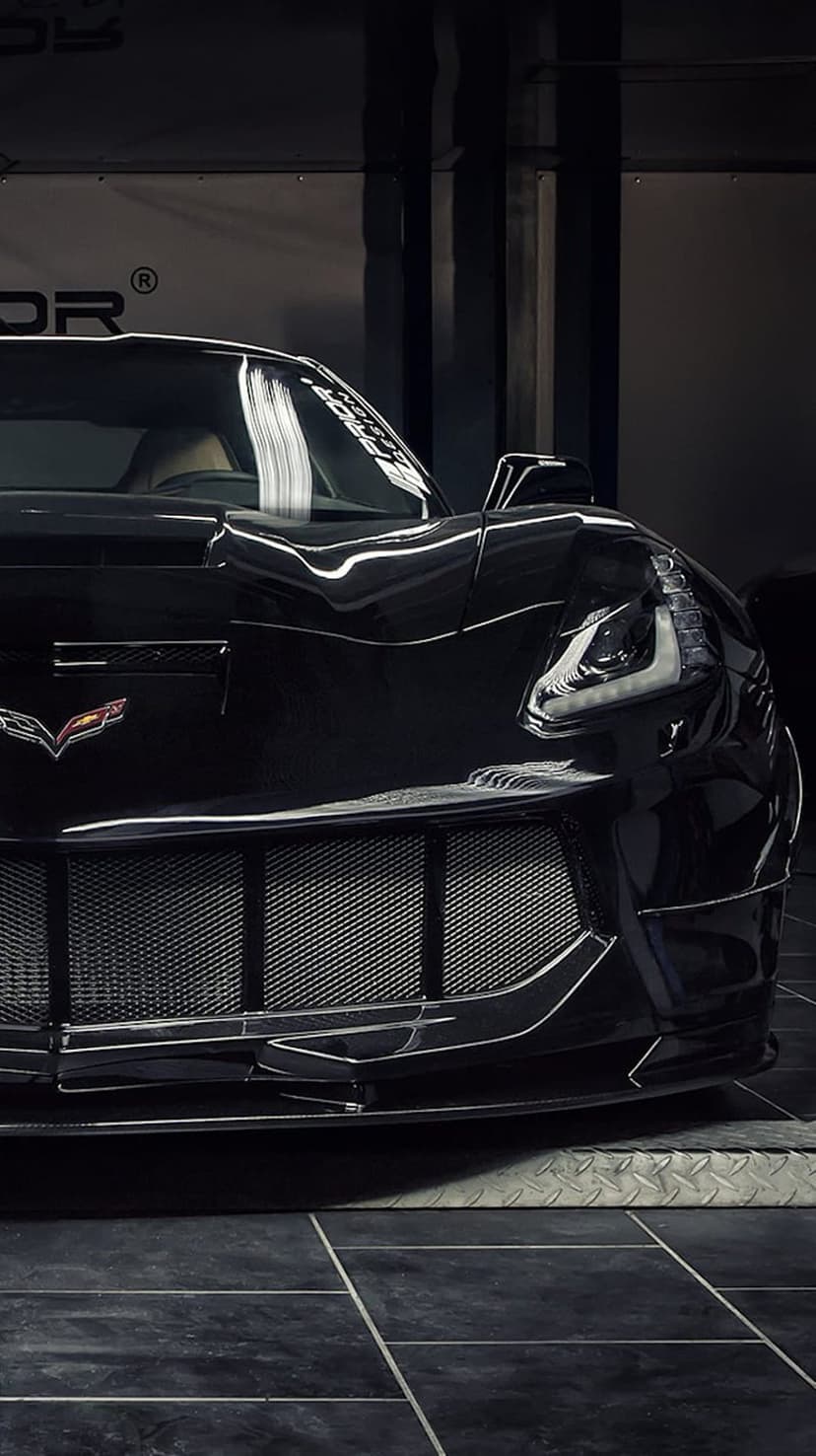 Black Corvette ZR1 with a glossy finish and sharp headlights sits in a dimly lit garage at a low-angle view.