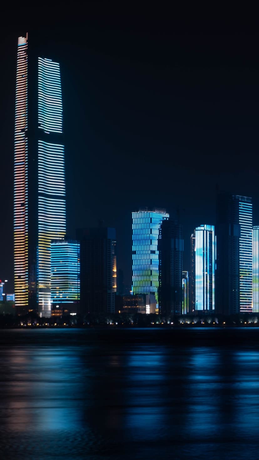 Neon skyscrapers in a futuristic city reflect on dark water at night under a clear midnight sky.
