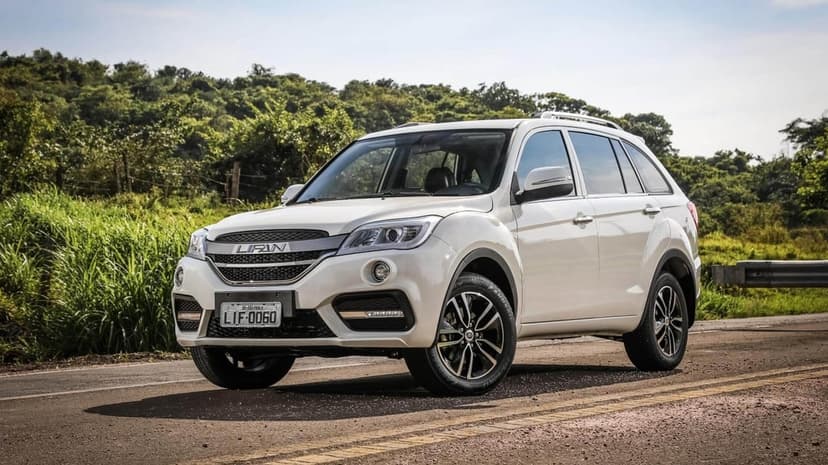 White Lifan X60 SUV parked on a paved road with lush green hills and trees in the background under bright daylight.