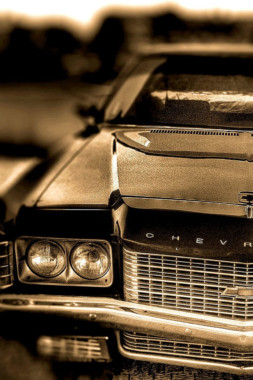 Classic Chevrolet front grille and round headlights captured in a sepia-toned close-up with metallic textures.