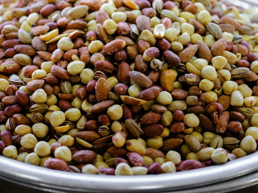 Whole almonds and cracked pistachios are piled together in a macro top-down view showing organic brown textures.