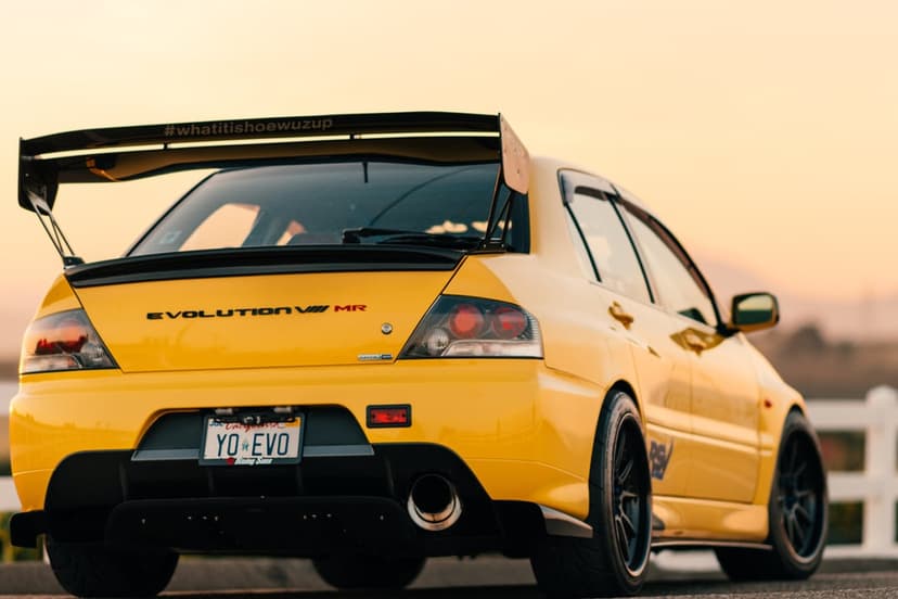 Yellow Mitsubishi Lancer Evolution IX MR with a large rear wing at sunset parked on a coastal road.