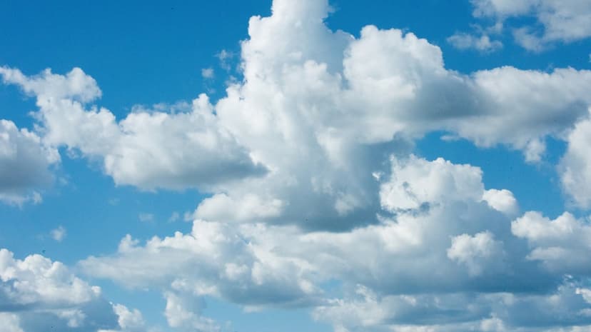 White cumulus clouds with sunlit edges float across a bright blue sky during a clear, sunny summer day.
