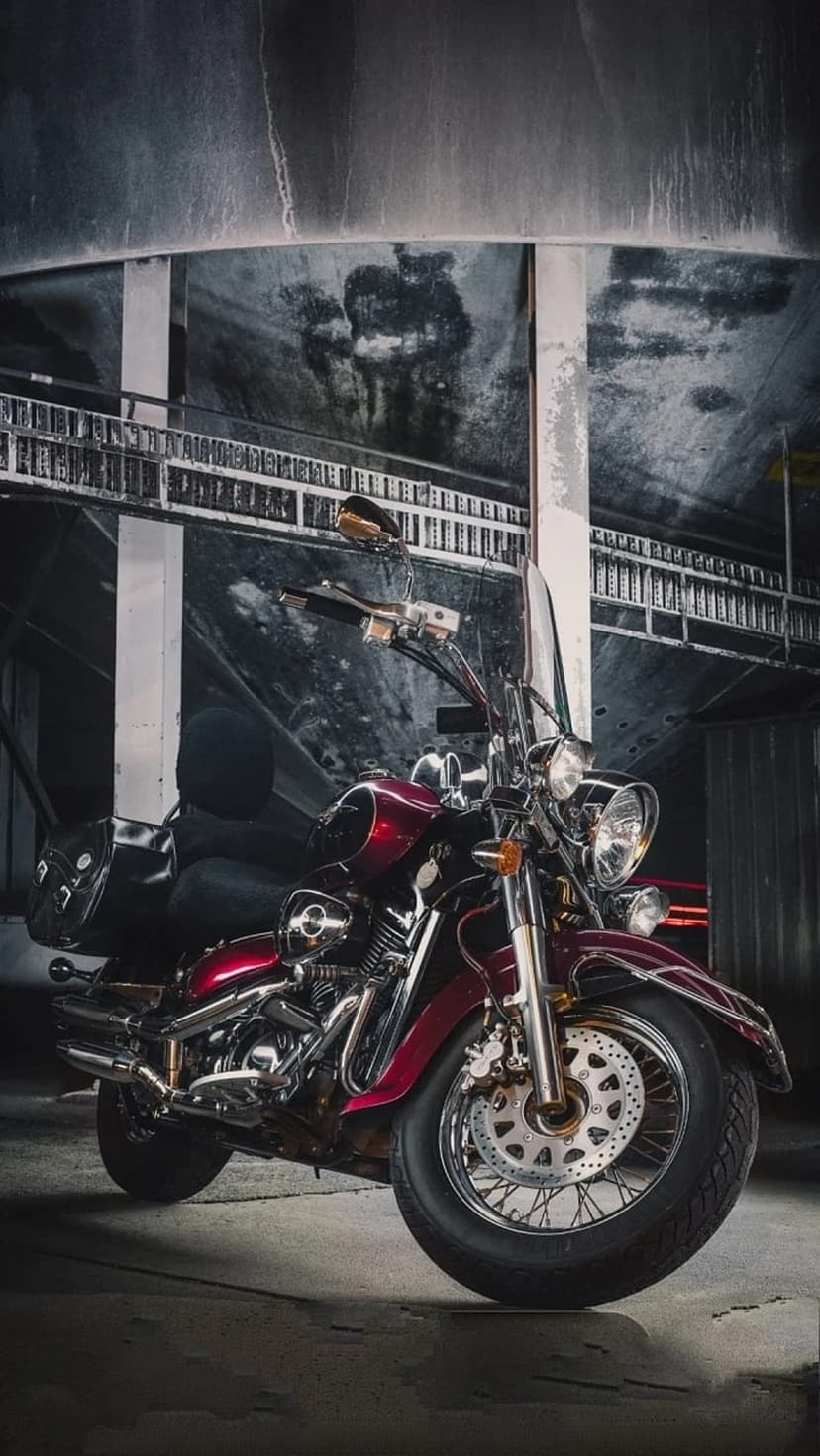 Cherry red cruiser motorcycle with chrome accents and a leather saddlebag parked in a dark industrial garage.