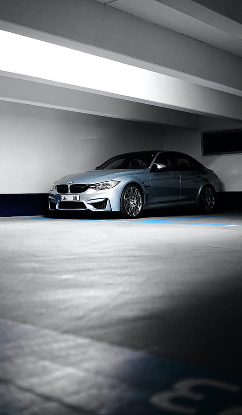 Silver BMW M4 coupe parked on a concrete garage floor under dim ambient lighting with visible alloy wheels.