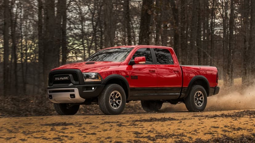 Red Ram 1500 Rebel pickup truck driving on a dusty dirt road through a dense forest of leafless winter trees.
