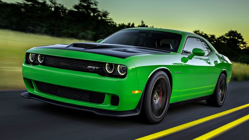 Green Dodge Challenger SRT Hellcat with a black hood driving on a road at sunset with motion blur.