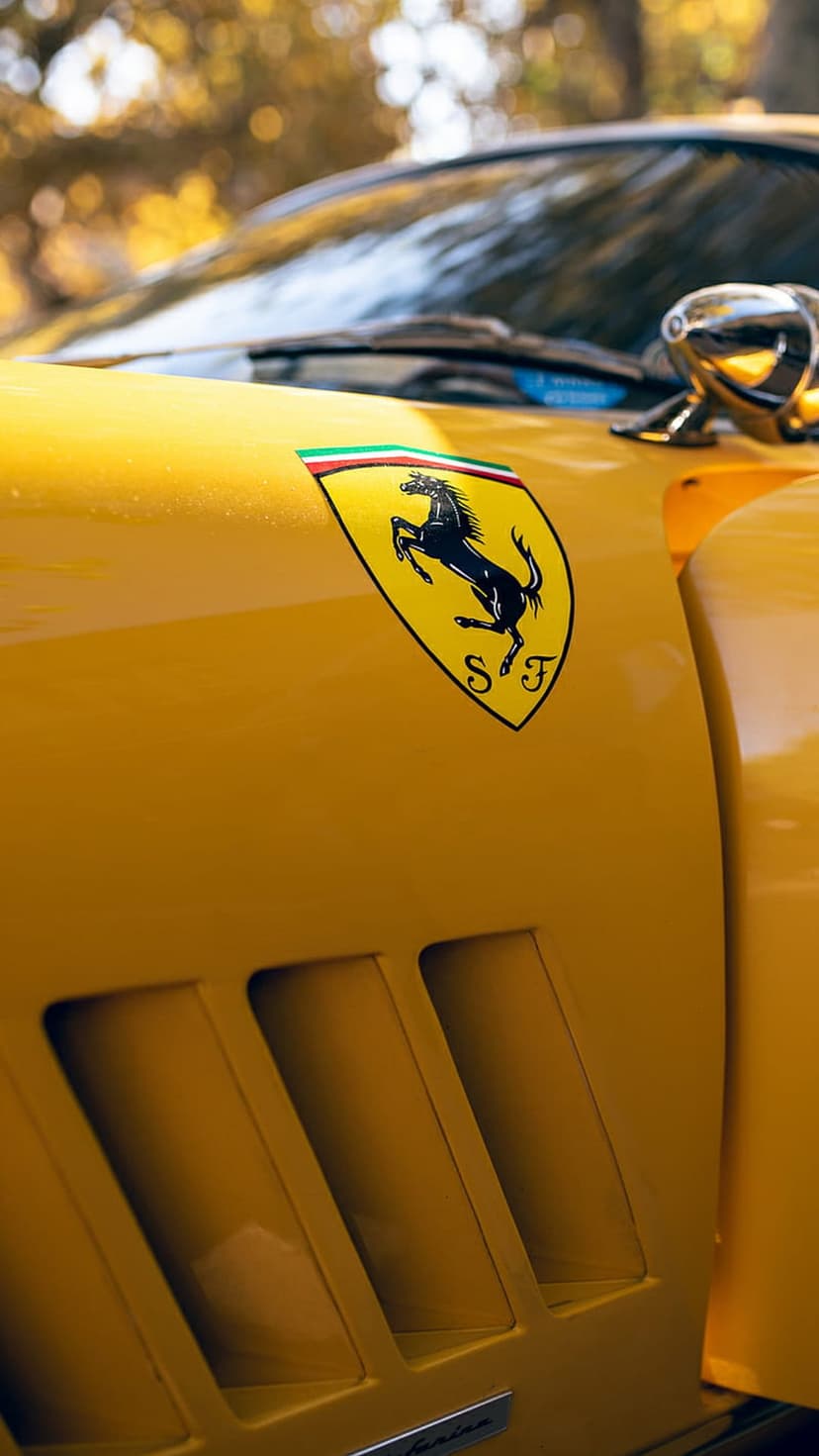 Silver Ferrari prancing horse emblem on a yellow metallic car body next to black aerodynamic air intake vents.