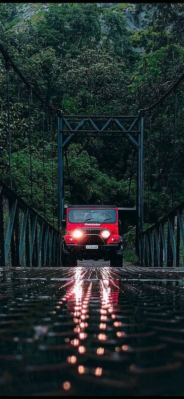 Red Mahindra Thar on a Wet Bridge Amidst Lush Greenery
